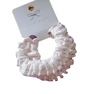 Polka dot cotton scrunchie with purple ruffled edges on white cardboard display card