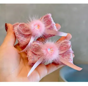 Close-up view of pink tweed bow hair clips with faux fur pom-poms and heart crystals