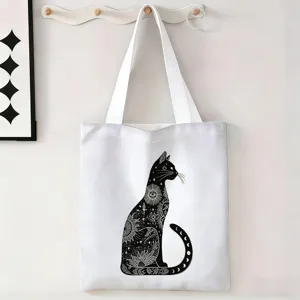 Vista detallada de una bolsa de lona blanca con estampado de gato místico colgada en un gancho.
