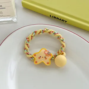 Detailed shot of a cute yellow star hair tie with rainbow braided elastic on a white plate