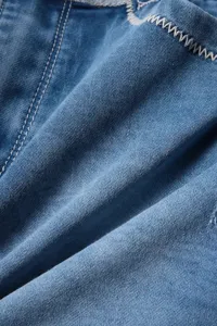 Λεπτομερής όψη μπλε denim υφάσματος με λευκές ραφές για γυναικεία καλοκαιρινή φούστα.