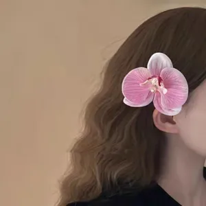 Close-up detail view of elegant pink orchid flower hair clip worn on wavy brown hair
