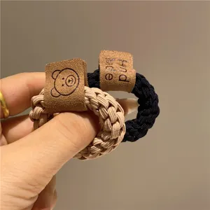 Dettaglio ravvicinato di elastici per capelli intrecciati con orsetto e logo Hand Made.