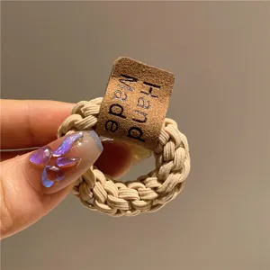 Dettaglio di un elastico per capelli intrecciato beige con etichetta in pelle