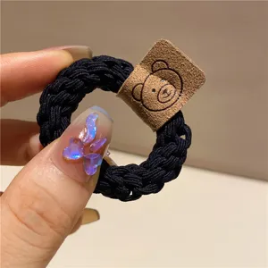 Primo piano di un elastico per capelli nero intrecciato con un simpatico orsetto su un'etichetta marrone.