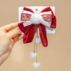 Detailed view of red velvet bow hair clip with embroidery and white pom-pom tassels