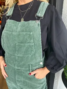 Detailaufnahme einer stilvollen grunen Kord Latzhose mit Fronttasche und glanzenden Metallteilen.