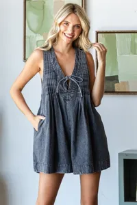 Détail de combinaison en denim lavé sans manches, avec plis devant, col V et poches pratiques.