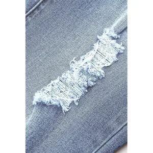 Close-up detail shot of light blue distressed denim fabric showing vintage washed ripped texture.
