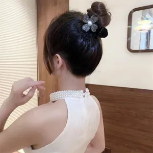 Detailed view of a sparkling rhinestone and pearl clover hair claw clip on a hair bun.