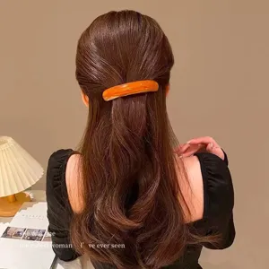 Elegant orange acetate hair barrette shown on long wavy hair in a warm interior setting.