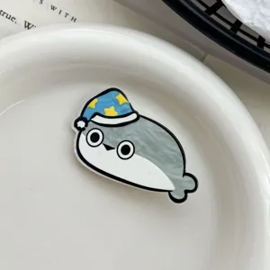 Close-up view of a cute cartoon Sacabambaspis acrylic hair clip on a white ceramic plate.