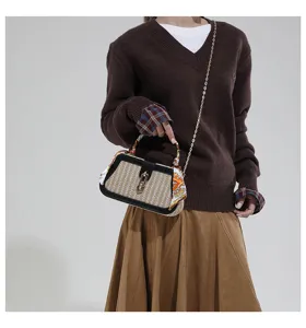 Elegante borsa a scatola in paglia intrecciata con finiture nere e tracolla a catena.