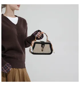 Dettaglio di modella che tiene una borsa in paglia intrecciata con finiture in pelle nera.