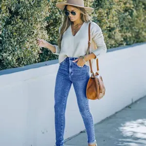 Detail view of women's stylish stretch skinny jeans paired with a casual sweater outdoors.