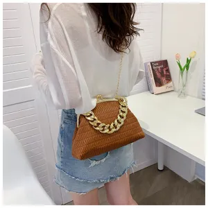 Eine Frau trägt eine braun plissierte Muscheltasche mit einer dicken goldenen Kette