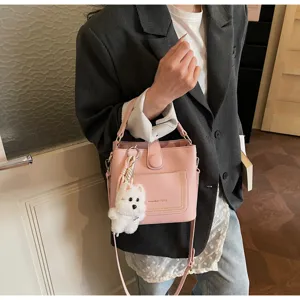 Sac seau rose à grain de litchi avec charmant chien blanc, porté par une personne.