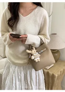 Lifestyle-Ansicht einer beigen Lederbeuteltasche mit Bärenanhänger und Schlossdetail.