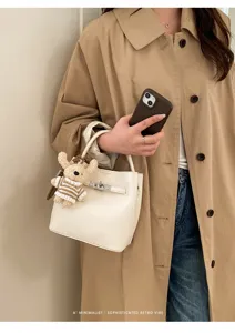Weiße Beuteltasche aus genarbtem Leder mit Schloss an Model im Trenchcoat.