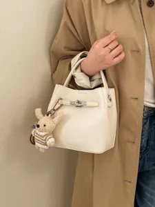 Minimalistische cremefarbene Eimertasche mit Schloss und süßem Bärenanhänger für Damen