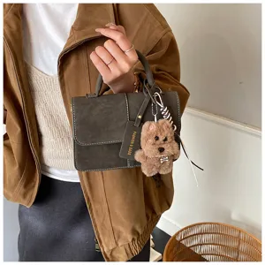 Close-up of vintage small square handbag with top handle and cute plush dog charm detail