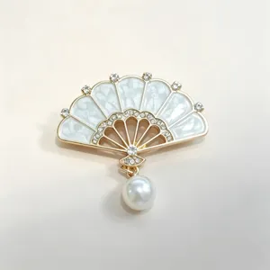 Close-up detail of elegant fan-shaped brooch with white enamel, rhinestones and pearl.