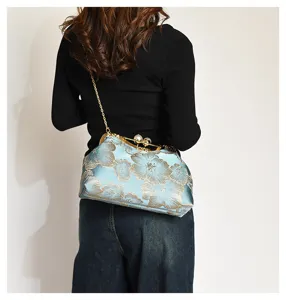 Vista de estilo de vida de un bolso bordado con flores azules, cadena oro y cierre perla.