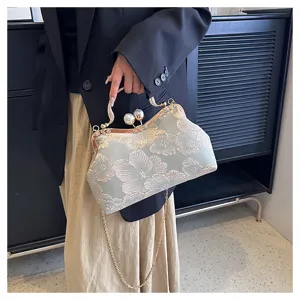 Detail of an embroidered floral handbag with decorative pearl clasp and chain strap.