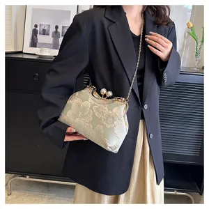 Vista detallada de elegante bolso bordado con cierre de perla y cadena de oro
