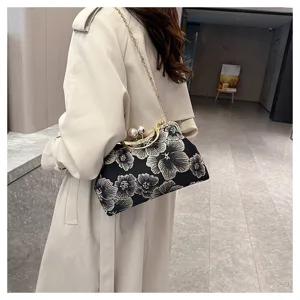 Detalle de un elegante bolso de mano bordado negro con cierre de perla en una modelo.