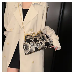 Vista detallada de bolso negro bordado con flores y cierre de perla sobre gabardina beige