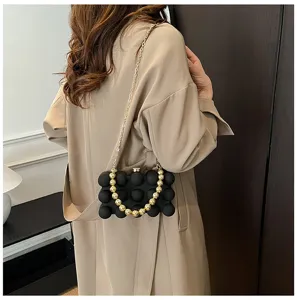 Detail einer schwarzen Bubble-Clutch-Tasche mit goldenem Perlen Griff und Kette