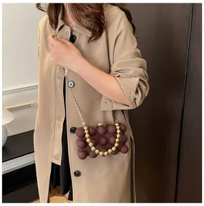 Braune Box-Tasche mit Perlenriemen, getragen von einem Modell in einem beigen Trenchcoat
