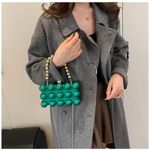 Nahaufnahme einer grünen Acryl-Bubble-Clutch-Tasche mit dekorativem goldenem Perlen Griff