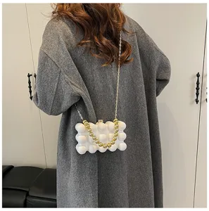 Rückansicht einer weißen Acryl-Blasentasche mit Goldkette über einem grauen Mantel