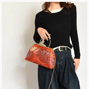 Detailansicht einer roten Vintage-Tasche mit Prägung, Goldverschluss und Kettenriemen