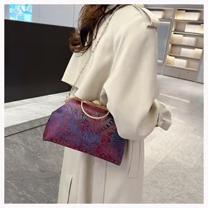 Detailansicht einer bestickten Muscheltasche mit Goldverschluss und Kettengurt am Modell.