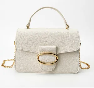 Detailed view of white pebbled leather handbag with gold oval buckle and chain strap