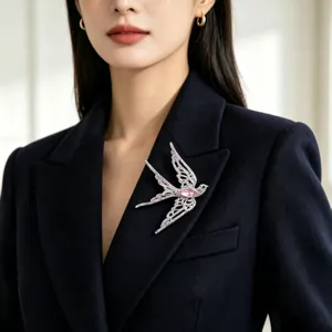 Detailed view of an elegant swallow brooch with pink crystal on a navy blazer.