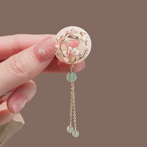 Close-up of elegant jade ring brooch with enamel magnolia flowers and gold tassels