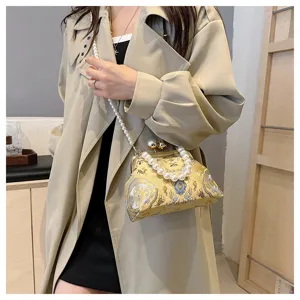 Elegante borsa ricamata con chiusura a scatto e manico di perle su un trench beige