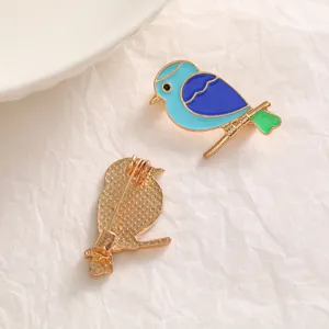 Detail view of an enamel bird brooch showing colorful front and back gold pin mechanism.