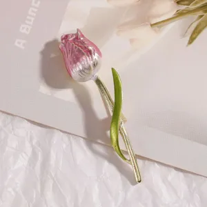 Dettaglio macro di un'elegante spilla a tulipano rosa con stelo dorato e foglia.