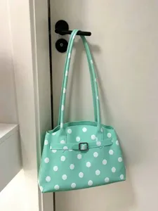 Primo piano di una borsa a tracolla in PVC verde menta a pois appesa a una porta