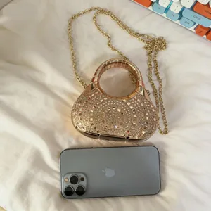 Mini bolso de noche con pedrería y cadena dorada junto a un móvil para referencia