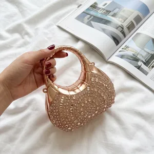 Elegante bolso de noche con diamantes de imitación oro rosa sostenido sobre fondo blanco