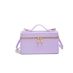 Elegant lilac crocodile embossed vanity handbag with top handle and gold zipper closure.