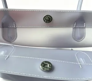 Detail of silver magnetic buckle and white stitching on lavender TPU waterproof bag.