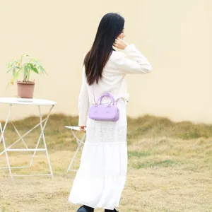 Elegante mini borsa a mano lavanda lucida abbinata a un abito bianco in un ambiente esterno.