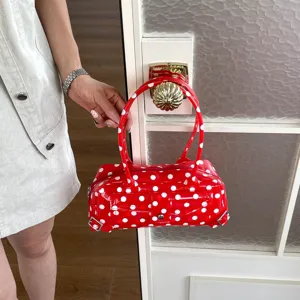 Close-up of a stylish red PVC handbag with white polka dots hanging on a door handle
